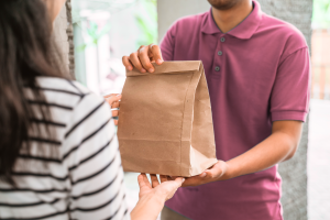 Delivery person handing over a paper takeout bag to a customer Elevating Delivery Experiences
