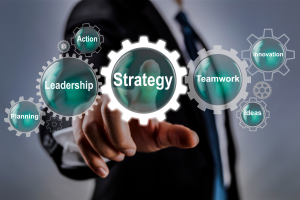 Businessperson interacting with digital gears labeled Strategy, Leadership, Teamwork, Planning, Innovation, and Ideas—representing elements of a cohesive marketing strategy.
