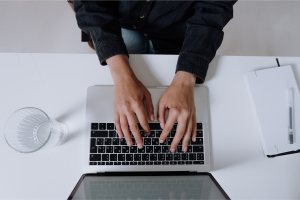 Person typing on laptop computer for blogging for business content creation at clean white desk workspace